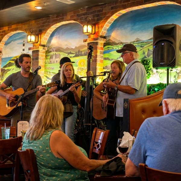 A band performs live music for diners in a restaurant with brick walls and scenic murals.