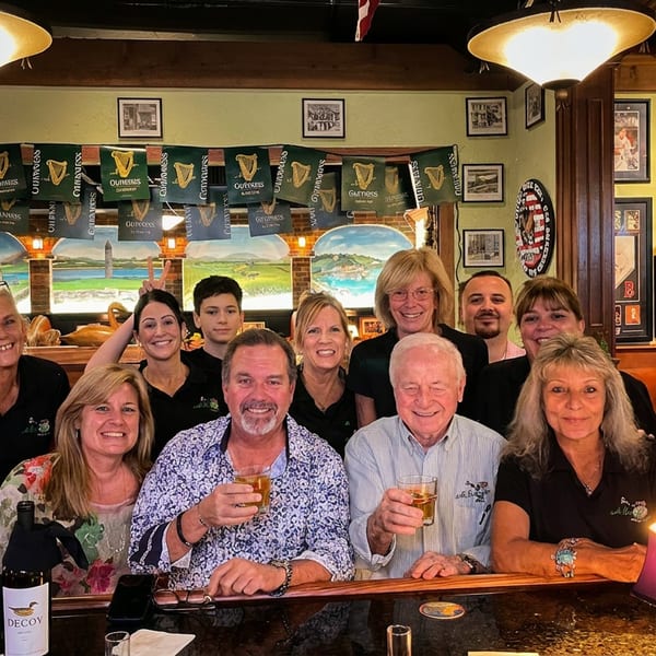 Smiling staff and patrons pose behind a bar with Guinness banners and Irish decor.