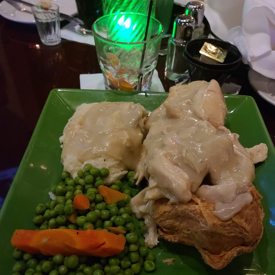 Chicken pot pie with mashed potatoes, peas, and carrots on a green plate at a restaurant.