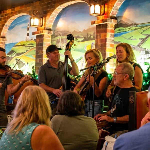 A band performs live music in a restaurant with brick arches and a scenic mural.
